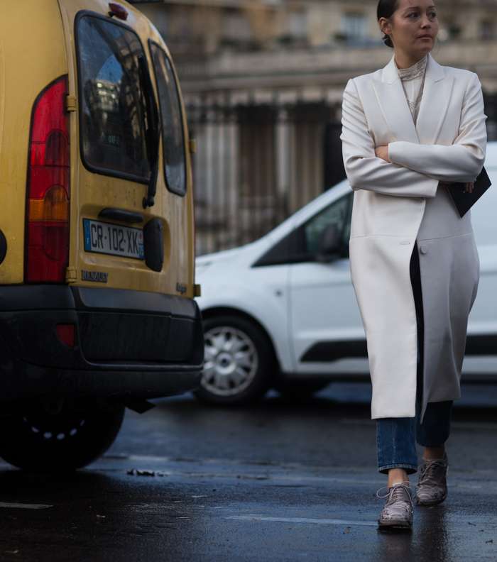 معطف أبيض كلاسيكي مع جينز وحذاء مسطح في شوارع باريس أثناء اليوم الأول من أسبوع الموضة الباريسي